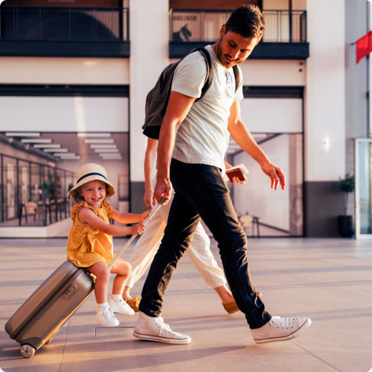 Man walking pulling a suitcase with a child sitting on it