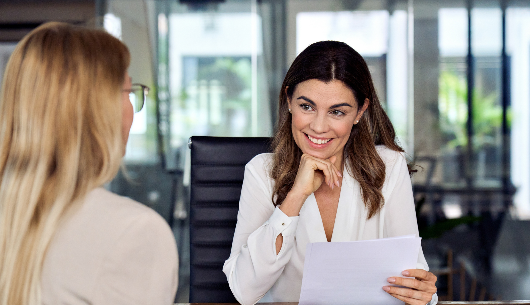 Happy mid aged professional business woman executive hr manager having job interview or business discussion with female applicant holding cv sitting at workplace in corporate office meeting.