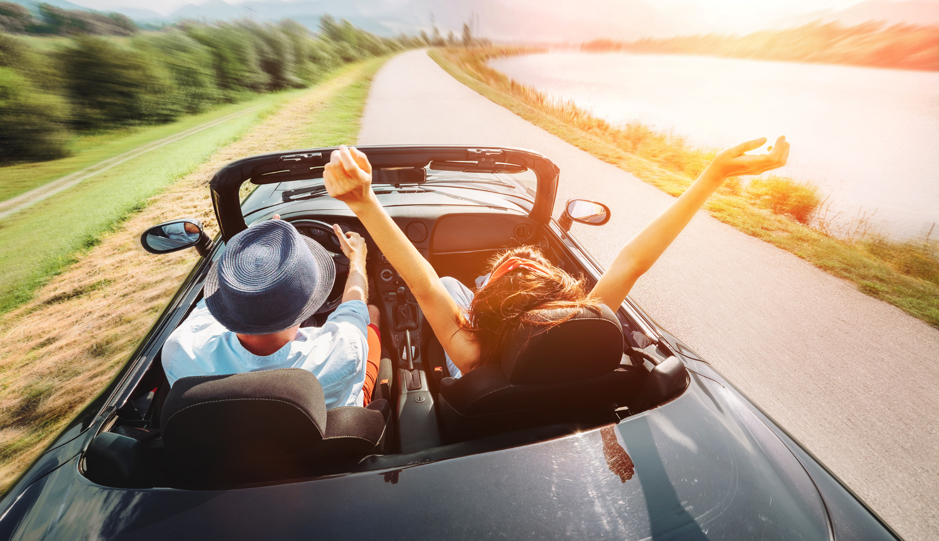 couple driving convertible with arms outstretched